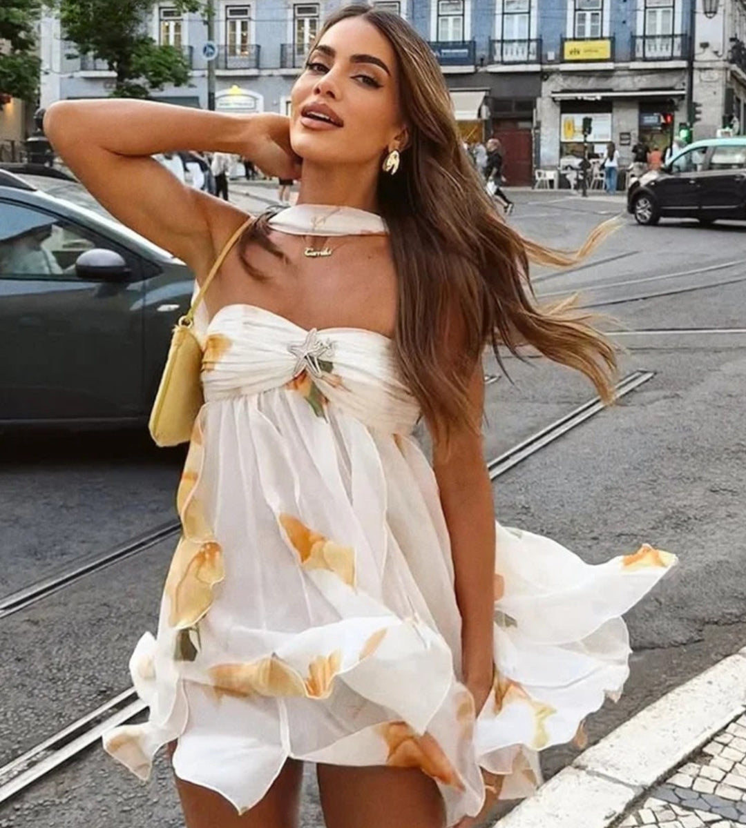 Modelo de frente usando o Vestido Curto Ischia com padronagem floral e aplicação no busto em cenário ensolarado.