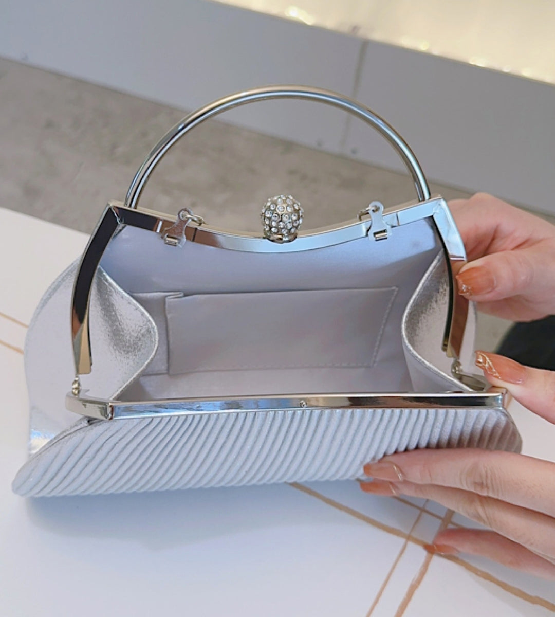 Detalhe da clutch dourada com alça de corrente removível e textura luxuosa em leque.