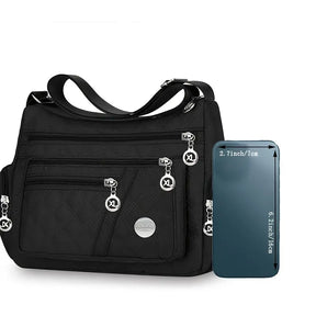 Bolsa feminina transversal preta ao lado de smartphone demonstrando tamanho compacto.