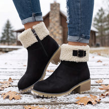 Bota feminina preta para inverno com forro peluciado, cano curto e sola tratorada em ambiente com neve.
