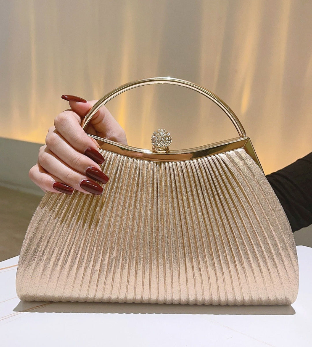 Clutch Milano champanhe plissada com brilho metalizado e fecho de cristal em destaque.