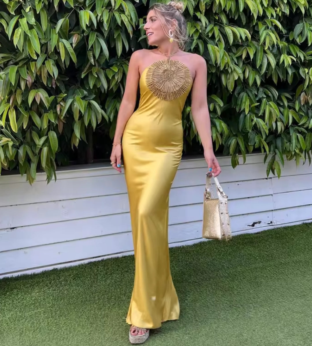 Mulher usando o Vestido Longo Aura com decote halter e aplicação floral bordada no busto em cenário luxuoso.