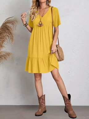 Mulher vestindo vestido curto soltinho mostarda com decote em V e babado na barra modelo Amalfi em vista frontal